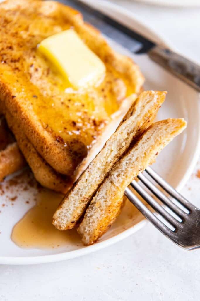 Fork holding slices of air fried french toast with slices of butter on top.