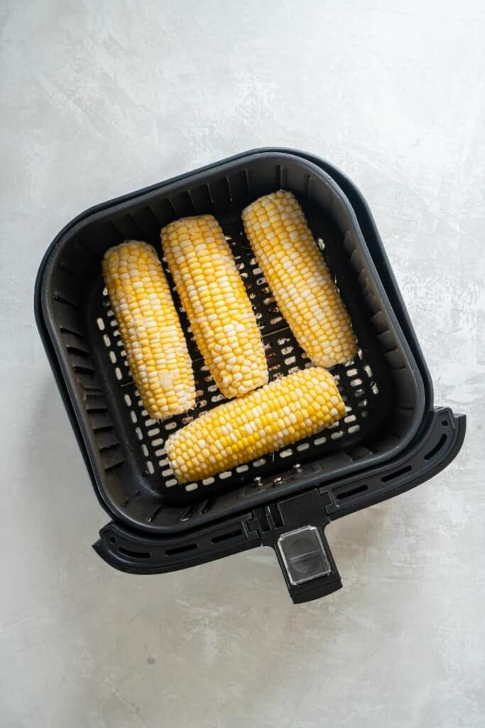 Overhead view of four unprepared ears of corn in a black air fryer basket.