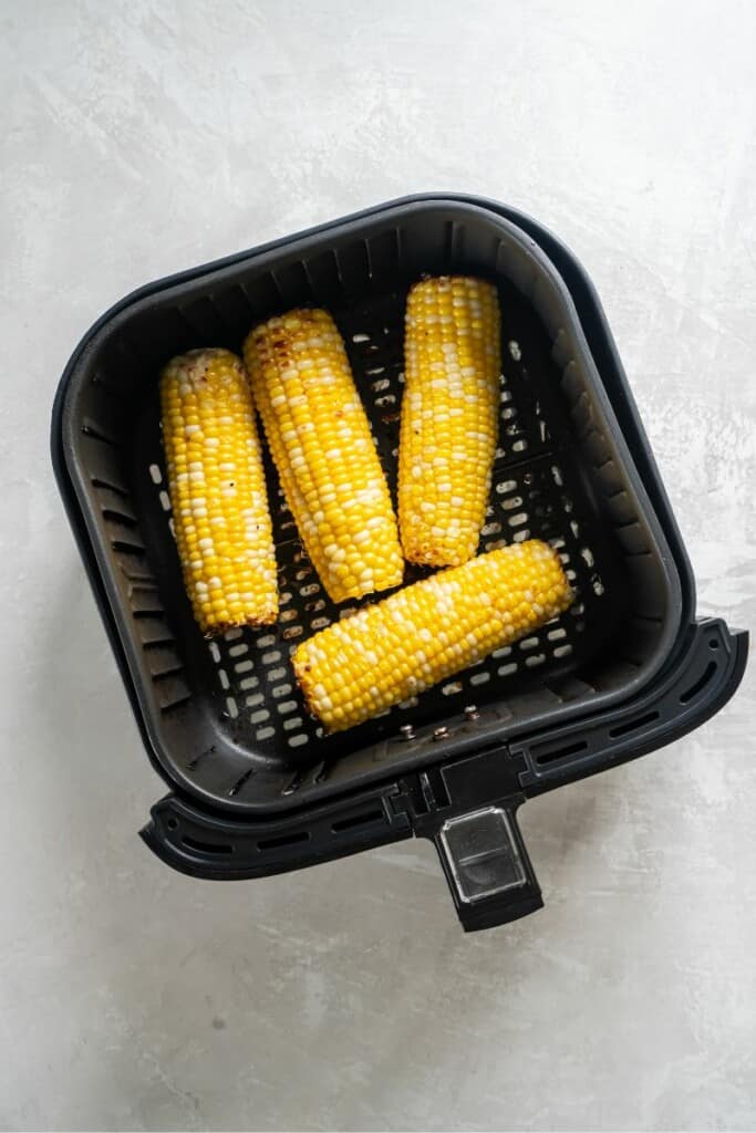 Overhead view of four prepared ears of seasoned corn in a black air fryer basket.