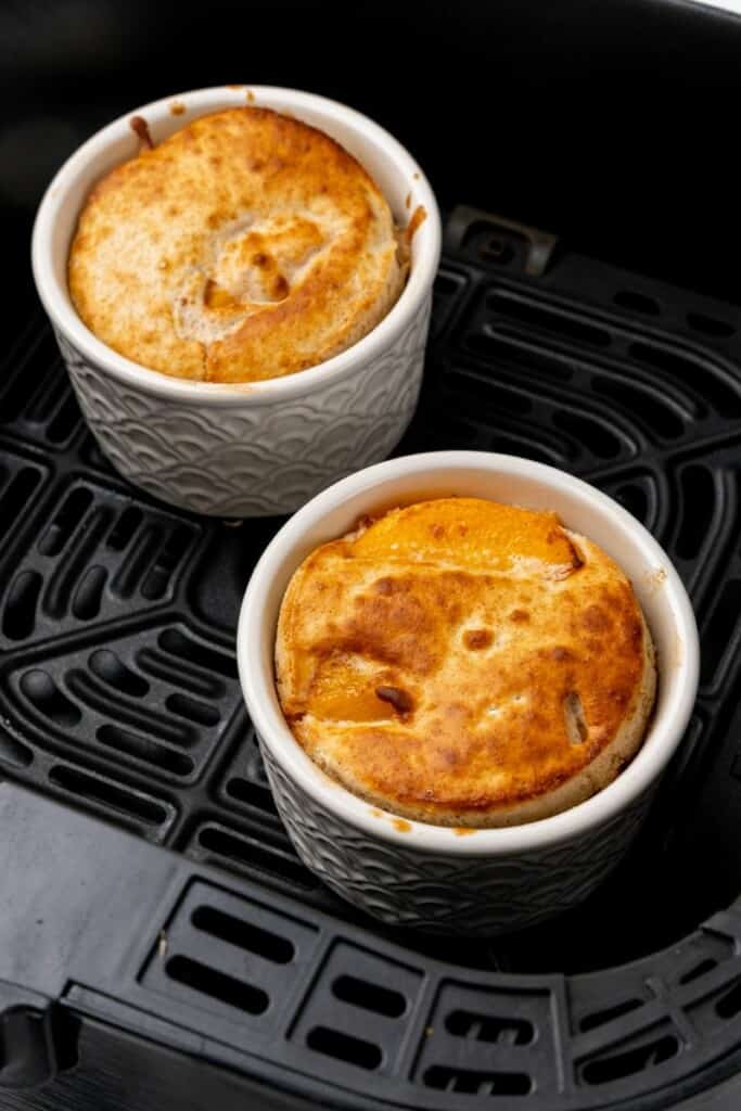 Close up view of two cooked peach cobblers in a black air fryer basket.