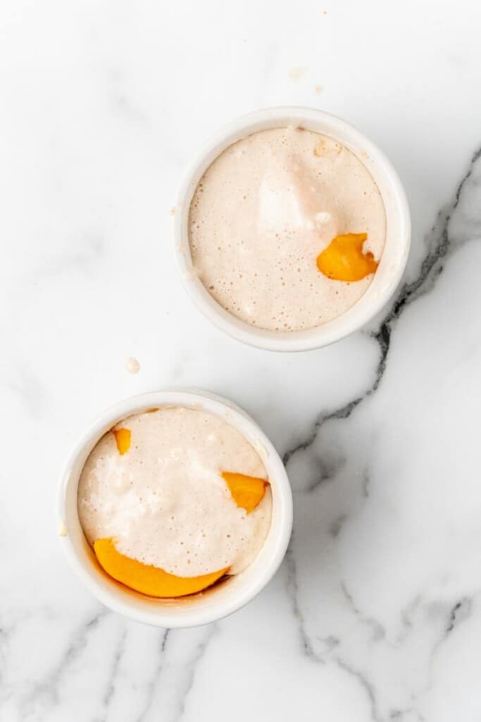 Pouring cinnamon bisquick mixture over peaches in ramekins.