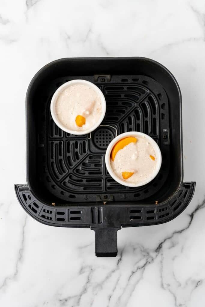 Uncooked peach cobblers in a black air fryer basket.