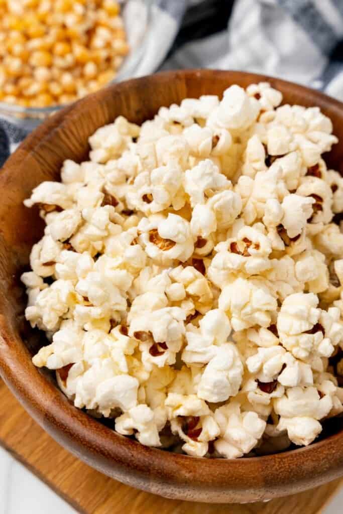 Closeup view of popcorn in a wooden bowl with kernels in the background.