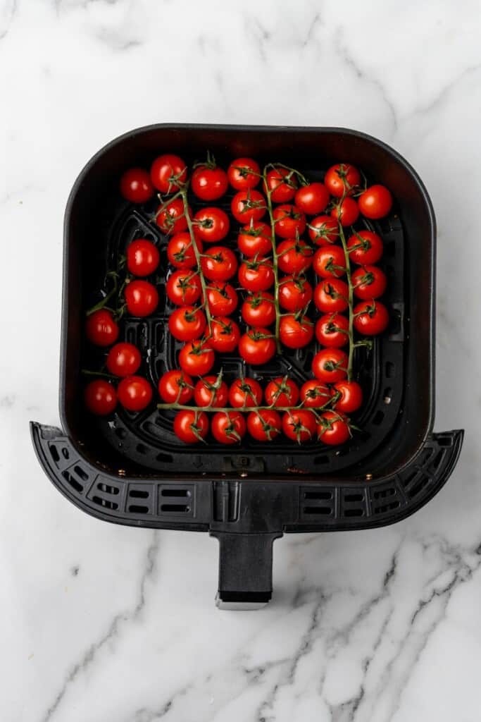 Cherry tomatoes in a black air fryer basket.