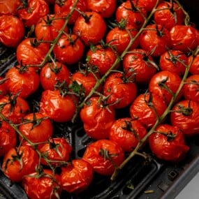 Seasoned cherry tomatoes that have been cooked in a black air fryer basket.