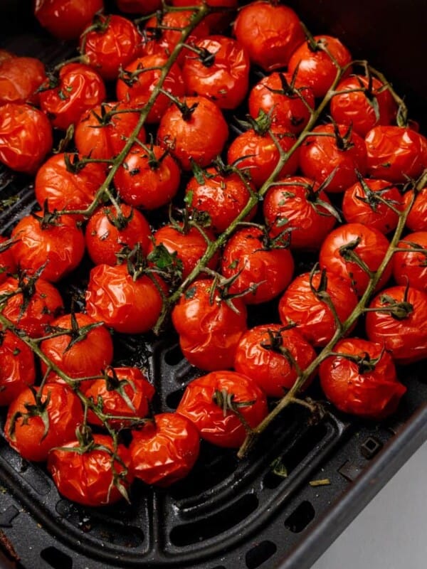 Seasoned cherry tomatoes that have been cooked in a black air fryer basket.