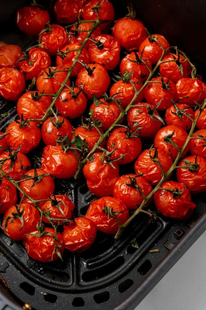 Seasoned cherry tomatoes that have been cooked in a black air fryer basket.