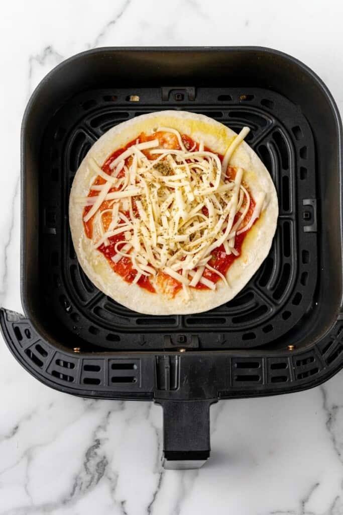 Cheese spread over sauce on tortilla resting in a black air fryer basket.