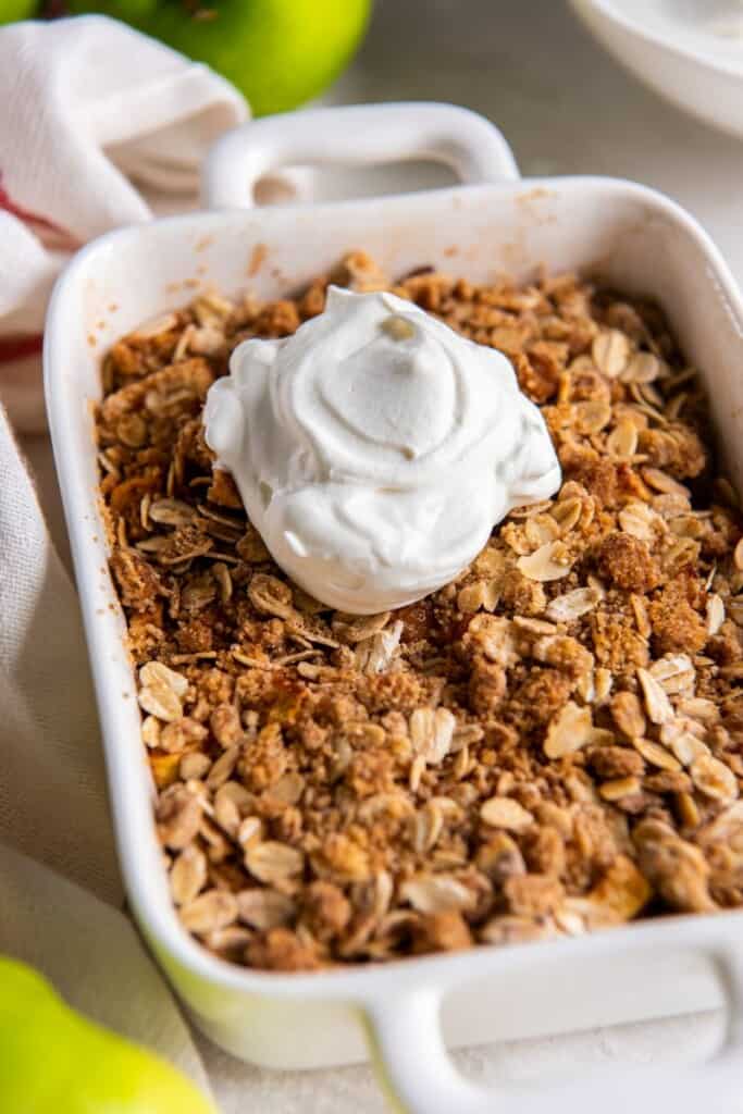 Prepared air fryer apple crisp in a white baking dish topped with whipped cream.