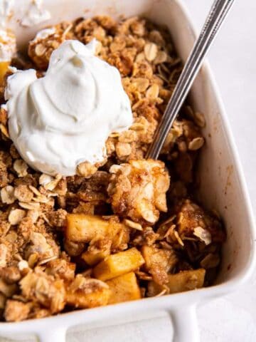 Spoon scooping a bite of prepared air fryer apple crisp in a white baking dish.