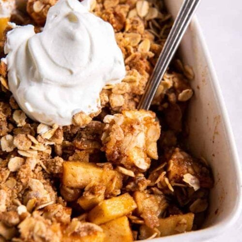 Spoon scooping a bite of prepared air fryer apple crisp in a white baking dish.