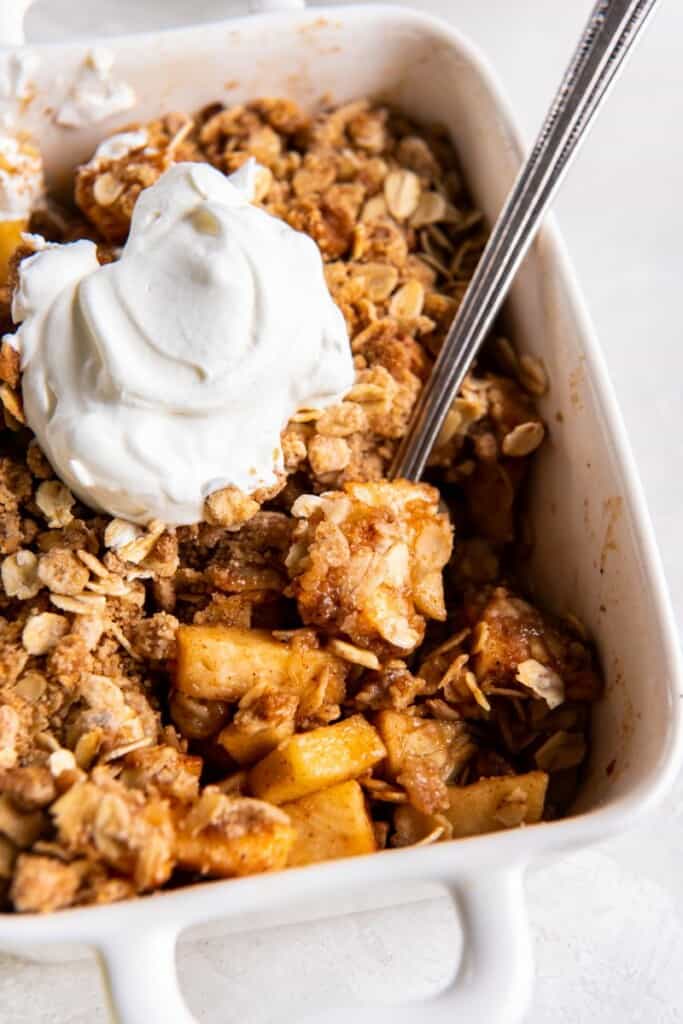 Prepared air fryer apple crisp in a white dish topped with whipped cream.