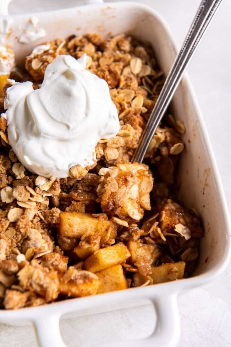 Spoon scooping a bite of prepared air fryer apple crisp in a white baking dish.