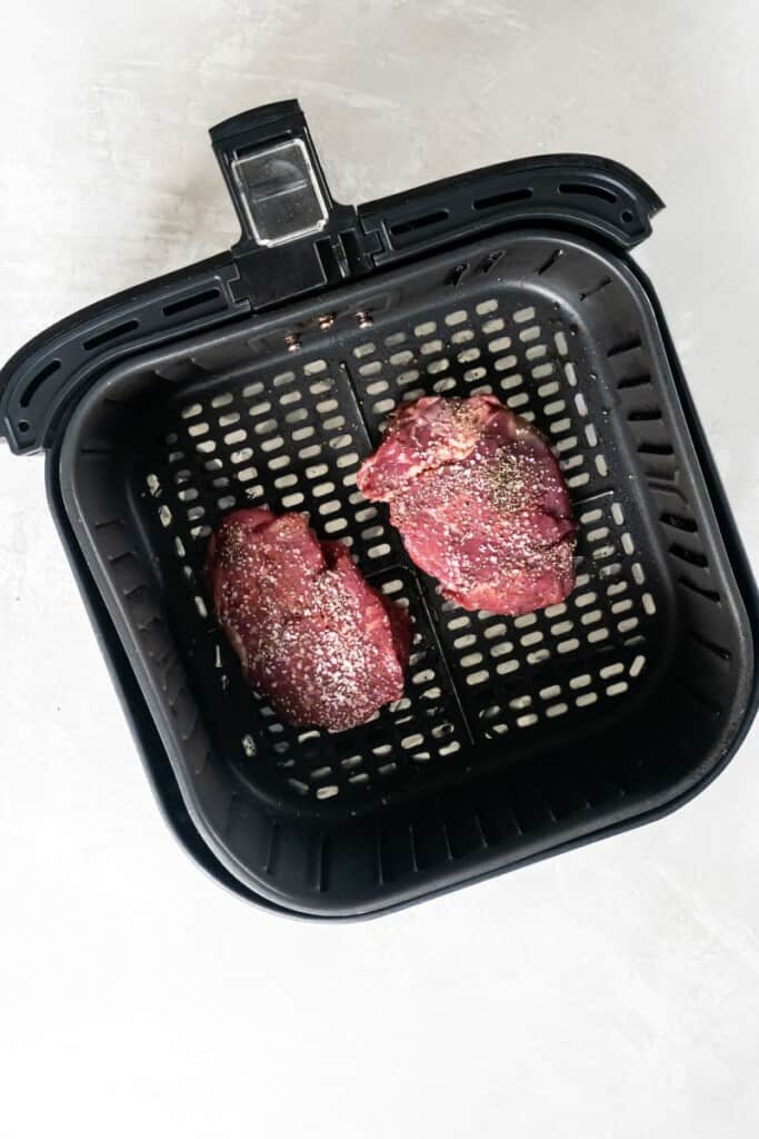 Two filet mignon steaks in a black air fryer basket.