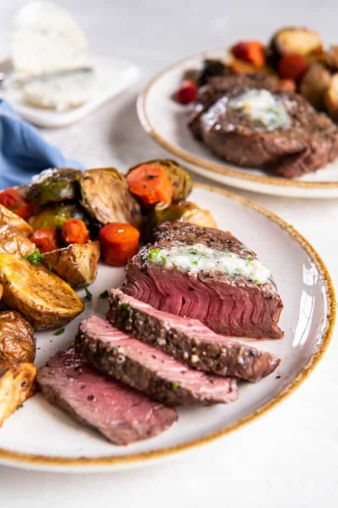 Slices of filet mignon with melted butter on a white plate with mixed vegetables.