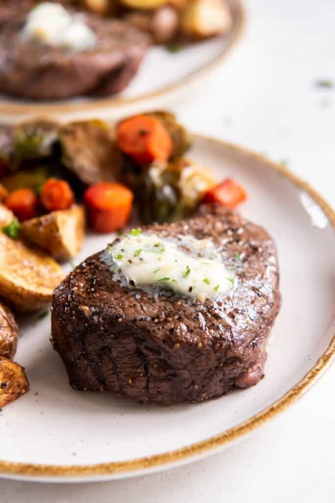 Whole air fried filet mignon with melted butter on a white plate with mixed vegetables.