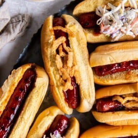 BBQ hot dogs with buns and toppings on a black platter.