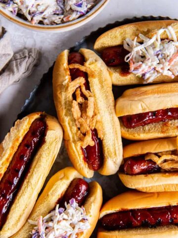 BBQ hot dogs with buns and toppings on a black platter.