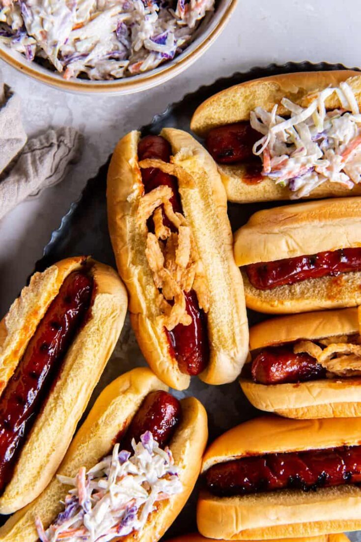 BBQ hot dogs with buns and toppings on a black platter.