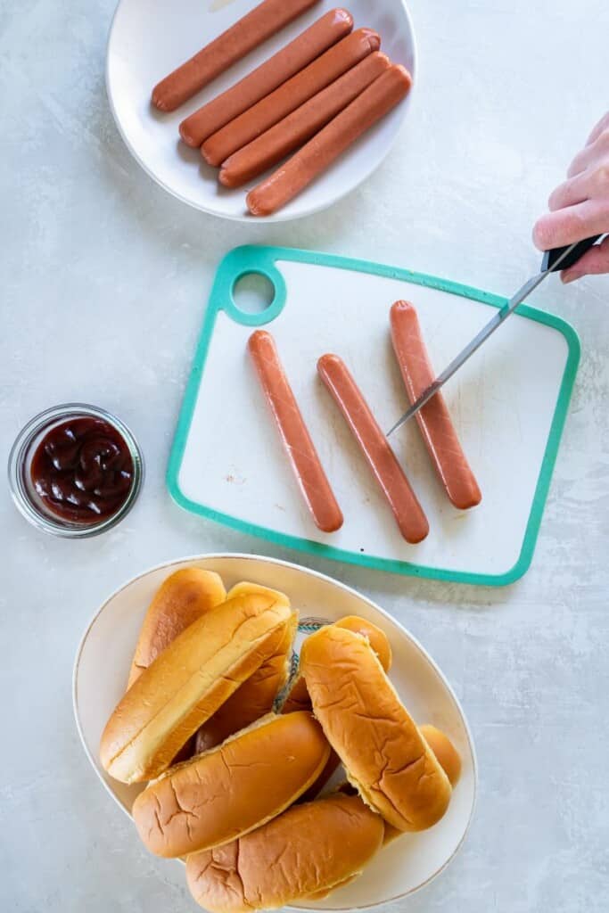 Using a knife to cut slices in hot dogs before grilling.