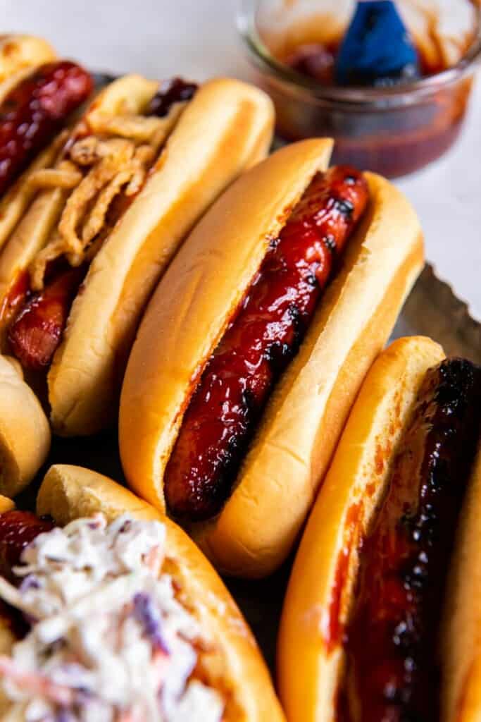 Grilled BBQ Hot Dogs in buns on a black plate.