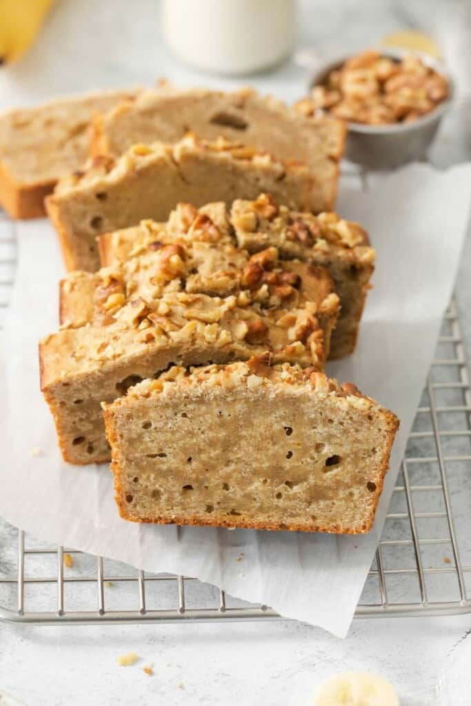 Baked banana bread cut into slices resting on a parchment lined cooling rack.