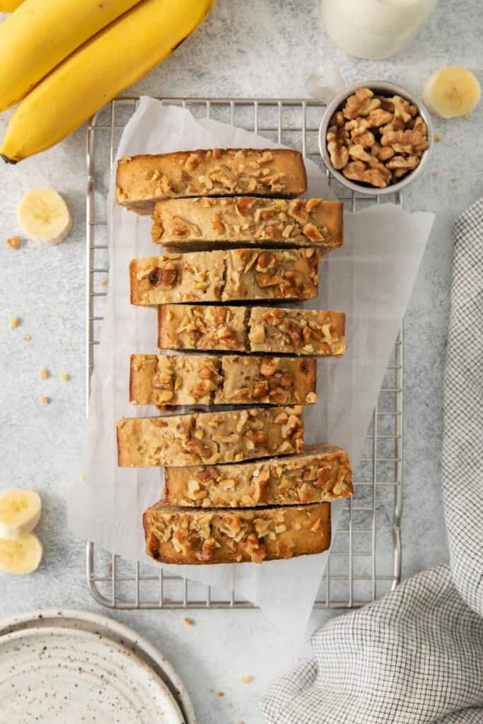 Loaf of banana bread cut into slices on a cooling rack.