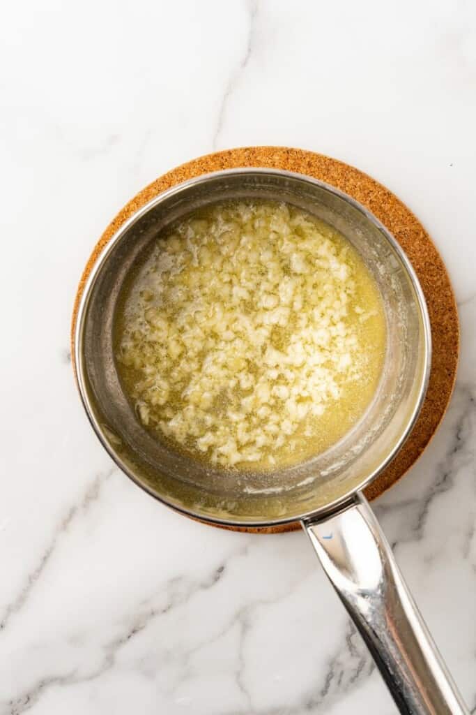 Melted butter and garlic cloves in a small sauce pan.