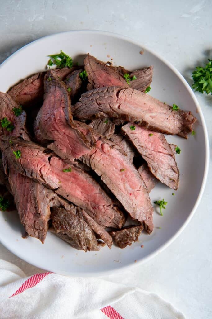 Slices of prepared flank steak cut into slices on a white plate.