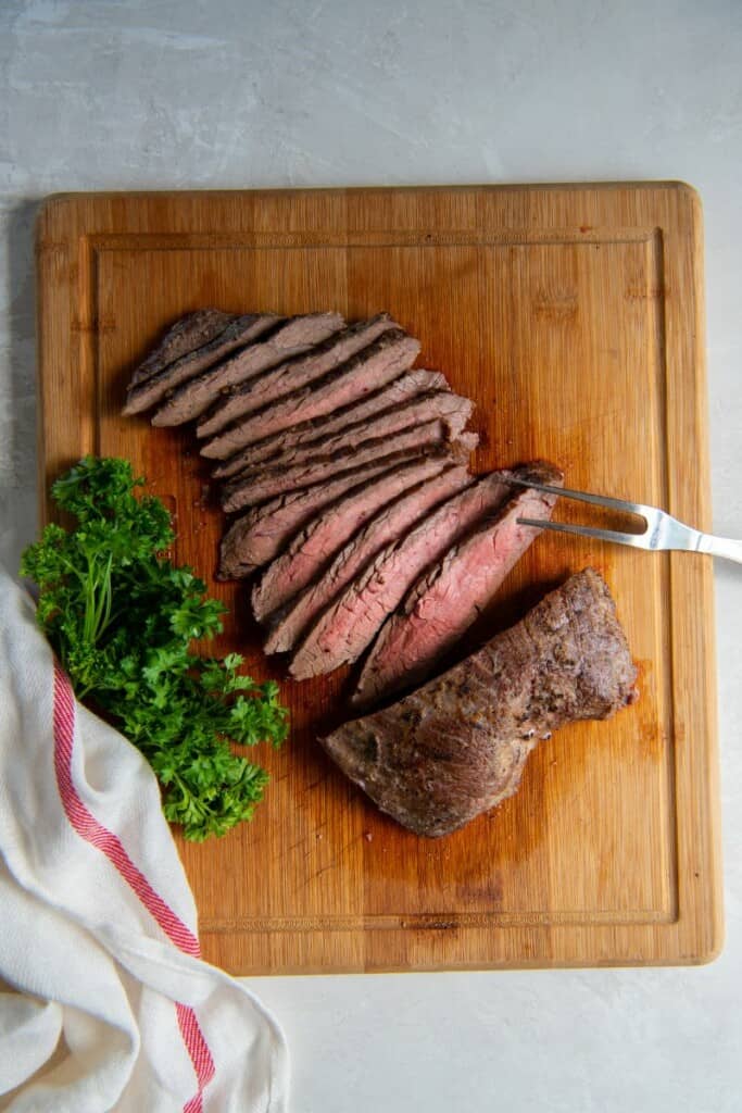 Slices of flank steak on a wooden cutting board.
