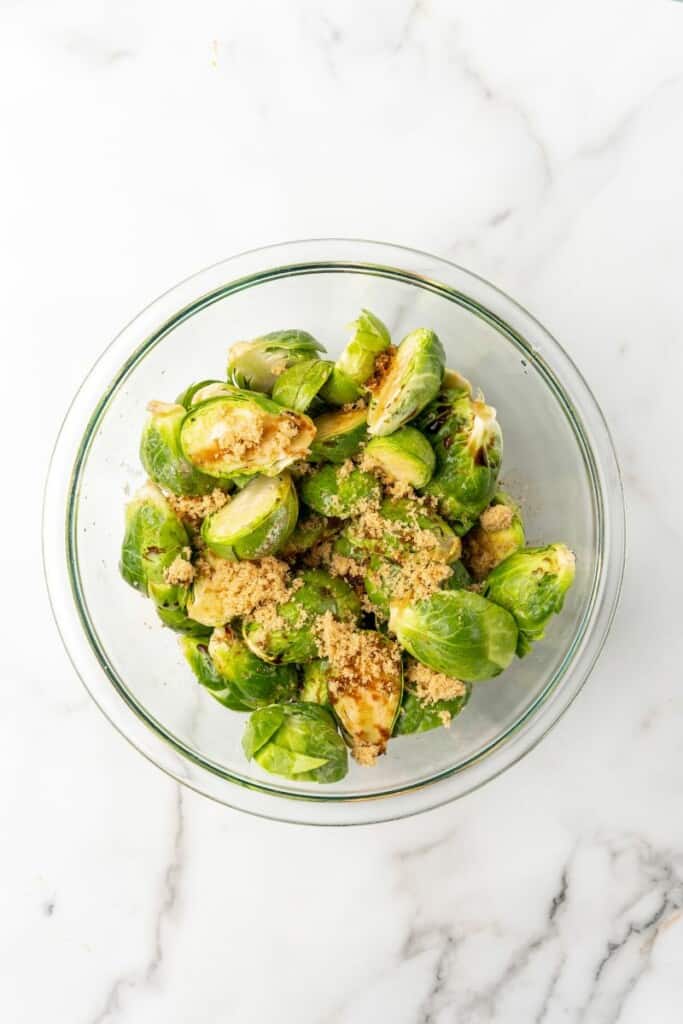Uncooked Brussels Sprouts coated in seasonings in a clear bowl.