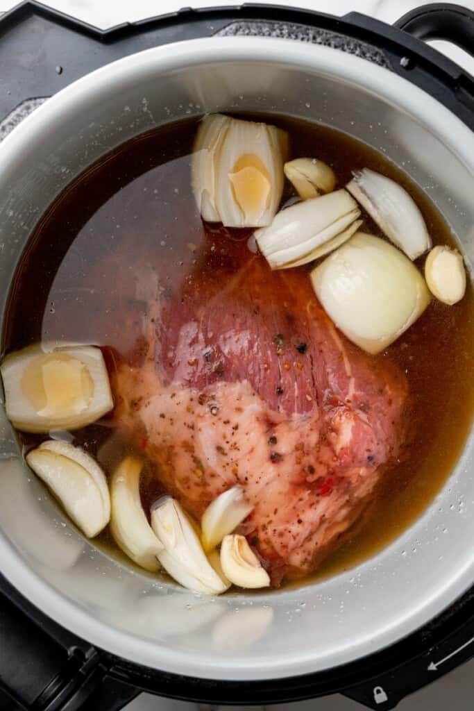 Beef broth with corned beef brisket, onions, and garlic cloves in a ninja foodi.