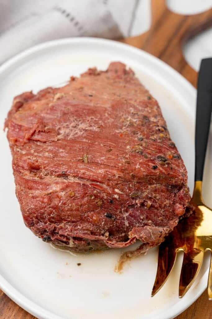 Fully cooked corned beef brisket on a white plate with a serving fork.