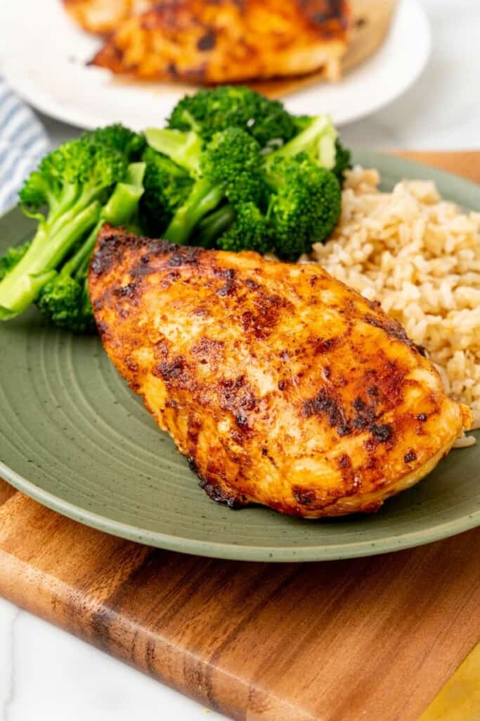 A chicken breast with broccoli and rice on a green plate.