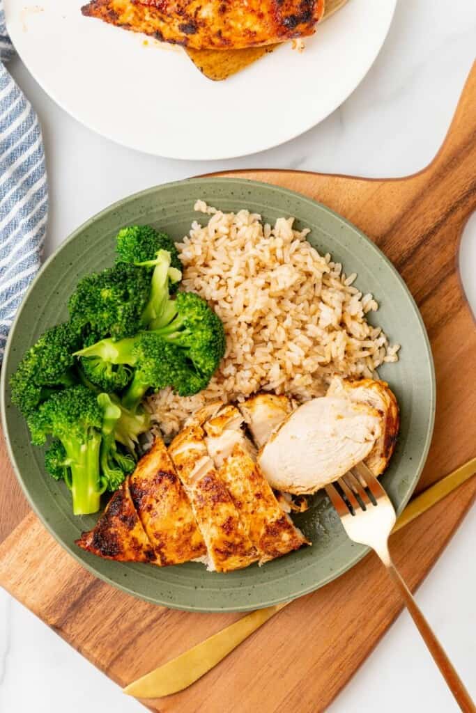 A seasoned chicken breast on a green plate with rice and broccoli.
