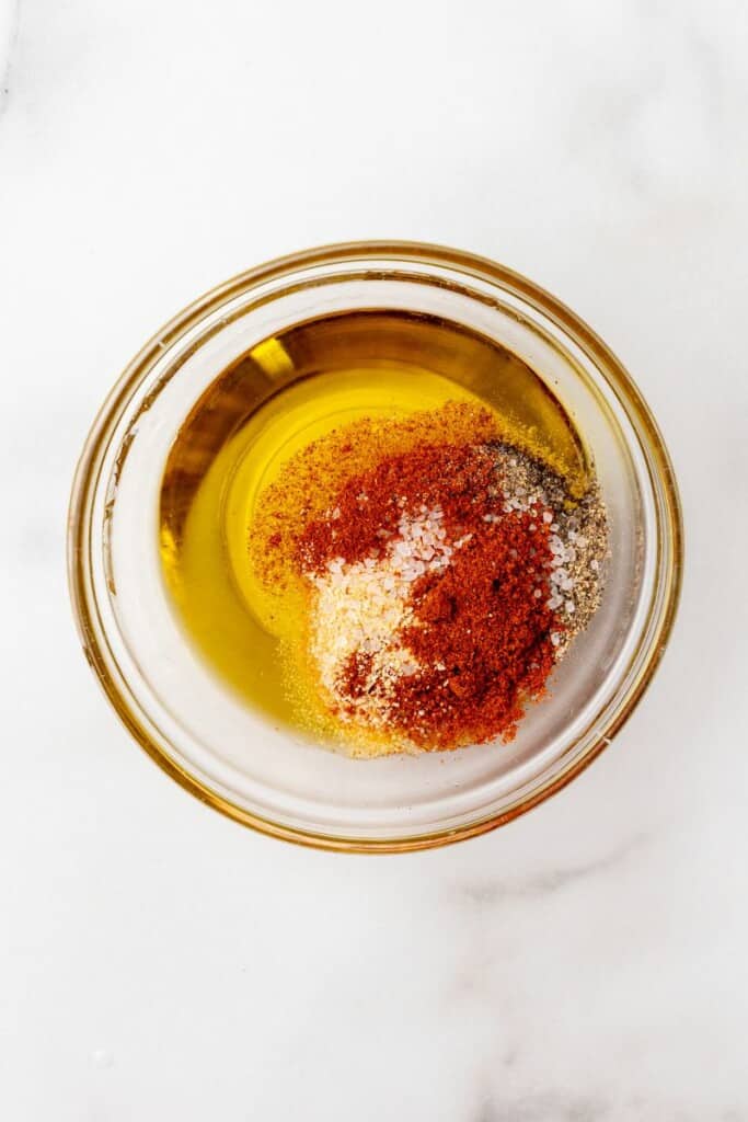 Mixing together paprika, Italian Seasoning, garlic powder, salt, pepper and oil in a small clear bowl.