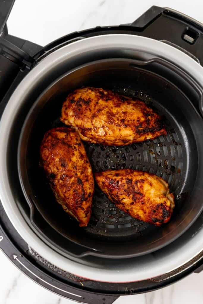 Three seasoned chicken breasts resting in a black ninja Foodi basket after being cooked.