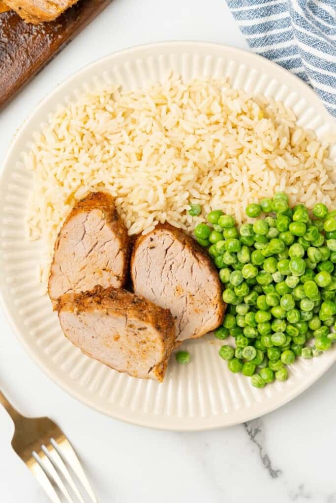 3 slices of pork tenderloin on a plate with rice and peas.