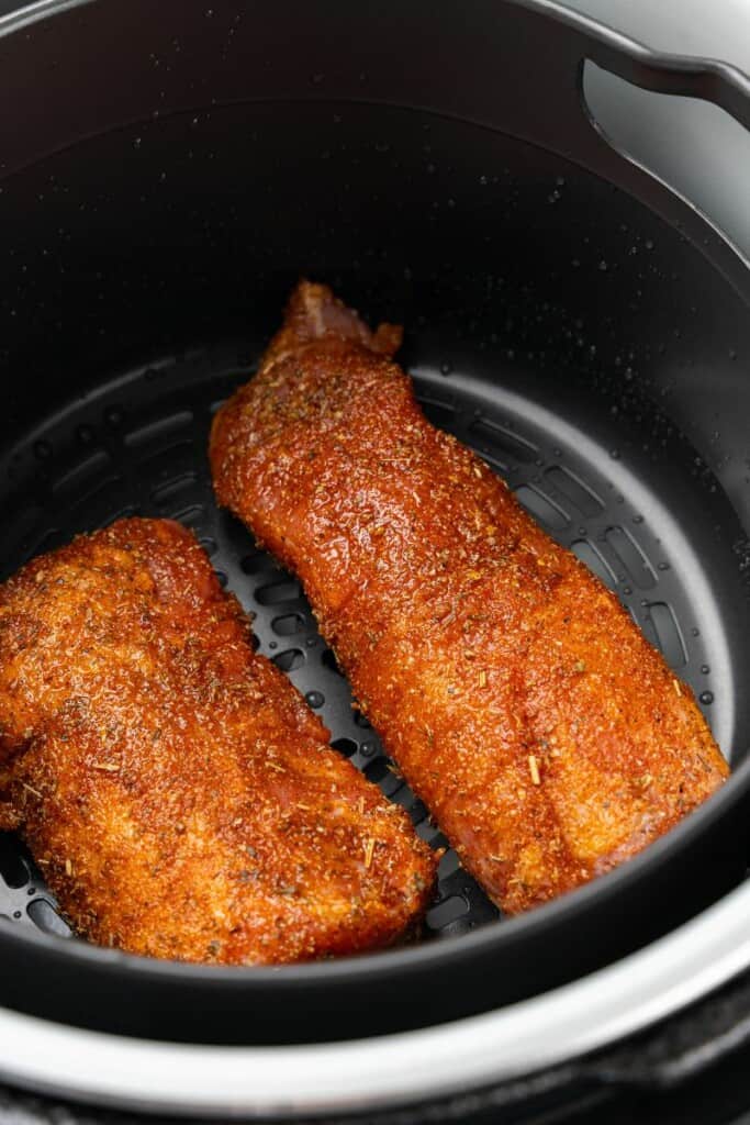 Seasoned pork tenderloin in a black ninja foodi basket ready to cook.