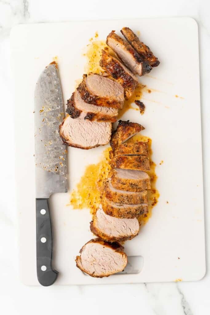 Overhead view of pork tenderloin cut into slices with a chef's knife.