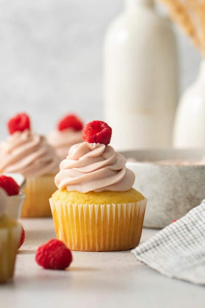 Cupcakes topped with fresh raspberry jam cream cheese frosting and a bottle of milk.