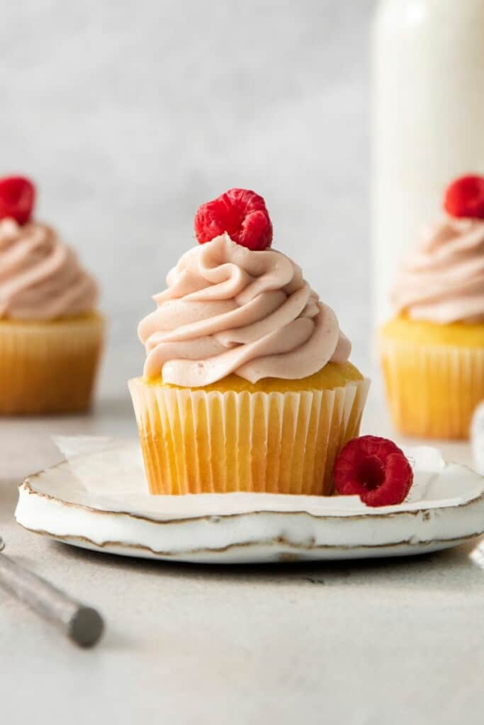 A close up view of a cupcake topped with fresh raspberry jam cream cheese frosting.