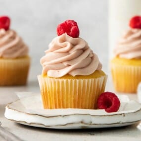 A cupcake topped with raspberry cream cheese frosting and fresh raspberries.