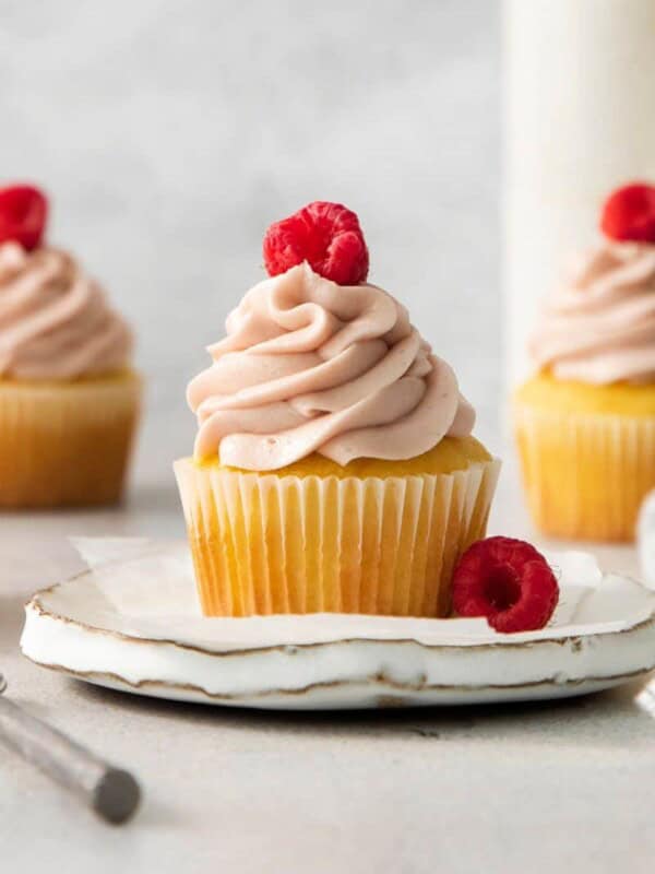 A cupcake topped with raspberry cream cheese frosting and fresh raspberries.