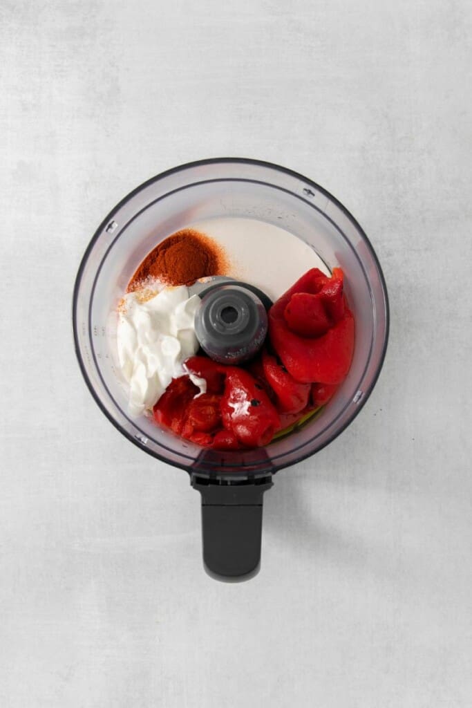 Overhead view of the ingredients needed to prepare smoky red pepper crema in a food processor.