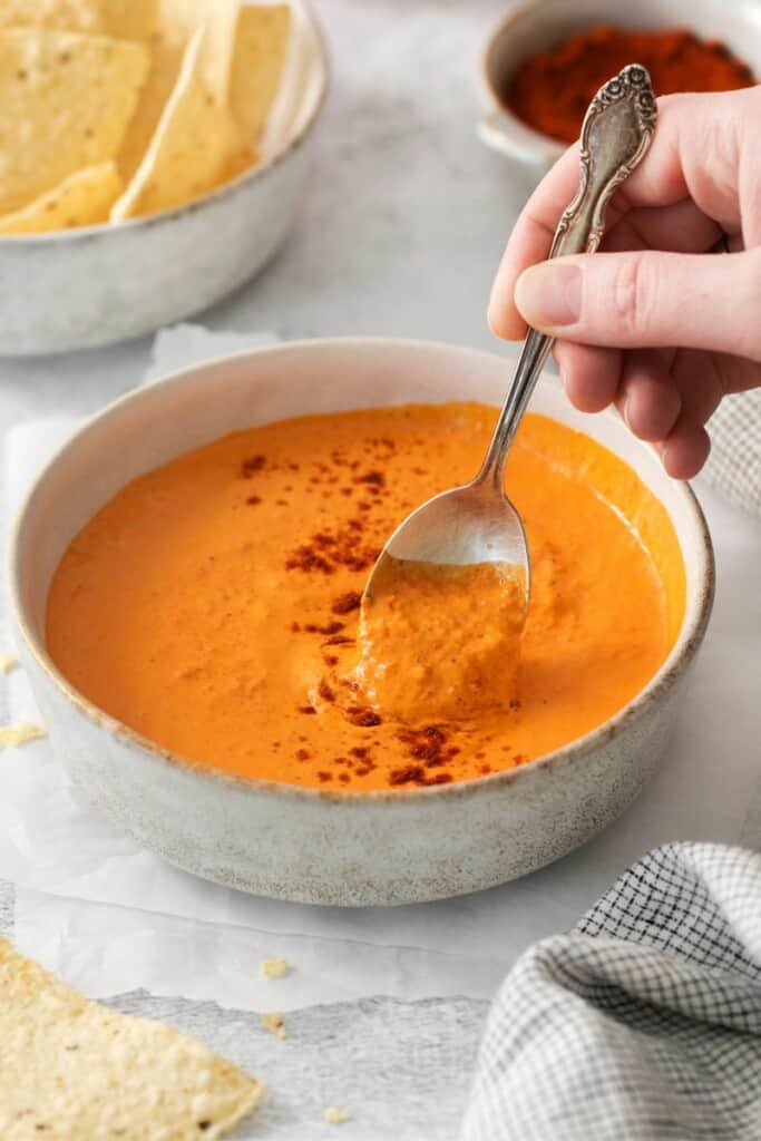 A spoon lifting a bite of red pepper crema out of a bowl.