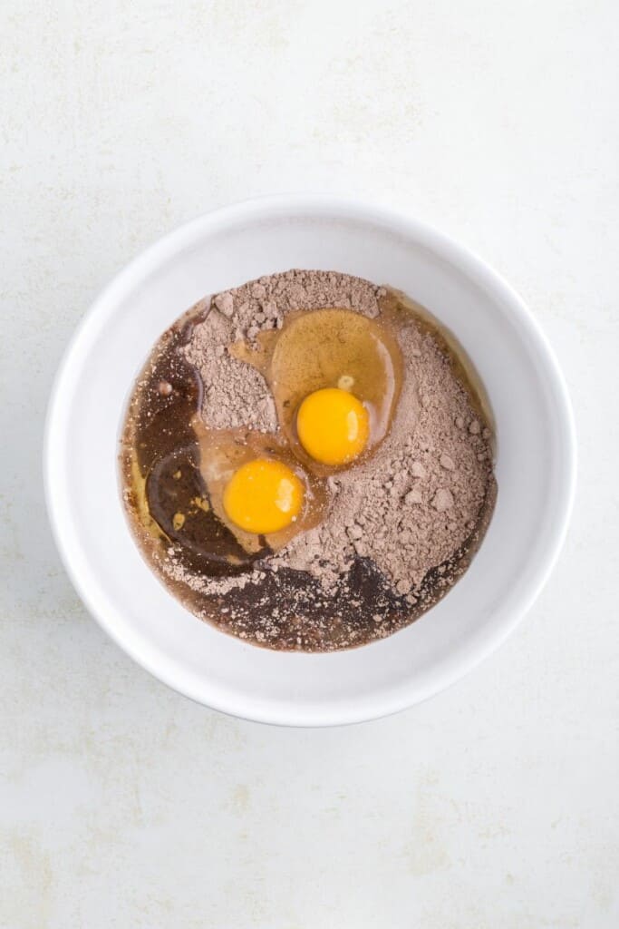 Overhead view of mixing cake mix, eggs and oil in a white mixing bowl.