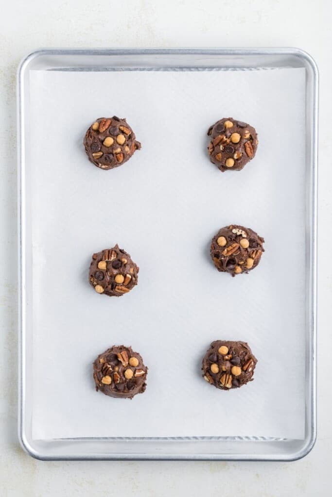 Overhead view of six scoops of cookie batter on a baking sheet lined with parchment paper.