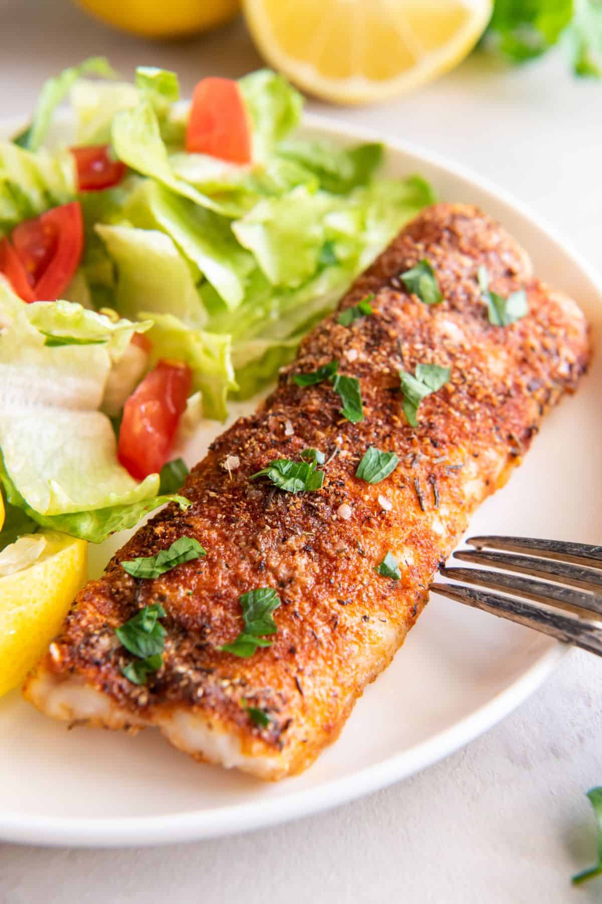 Air fryer frozen cod cooked and on a plate next to a salad.