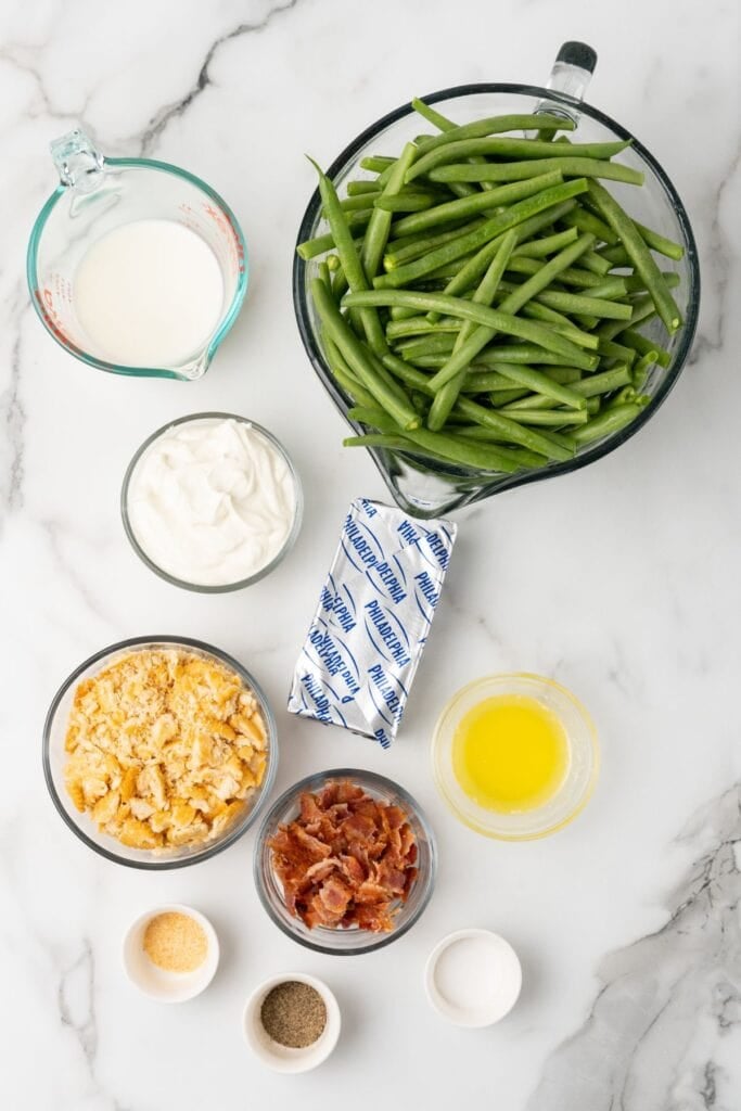 Ingredients needed to make green bean casserole with cream cheese: green beans, cream cheese, sour cream, milk, garlic powder, salt, Ritz crackers, butter, and bacon.